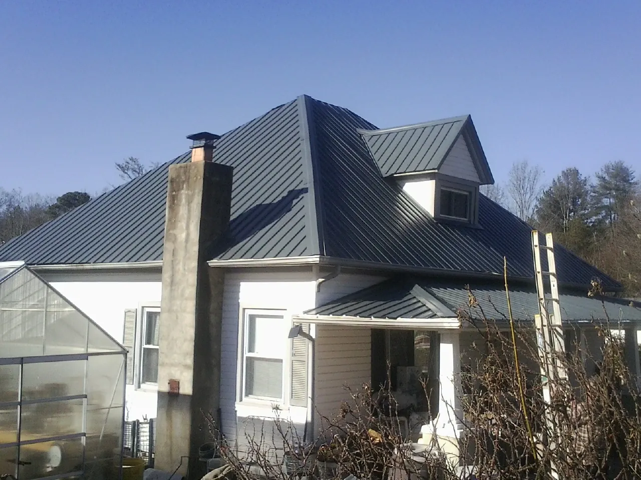 Dark blue standing seam metal roof on a white farmhouse with dormer — Slate & Tile Roof Repair by Roofing Brothers in Bath Springs
