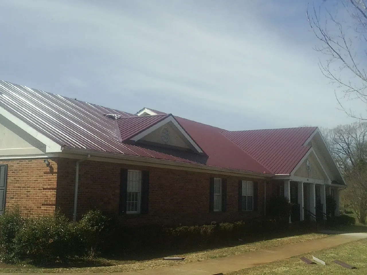 Red metal roof with gabled entries on a long brick building, from a Hail Damage Roof Repair job in Bath Springs