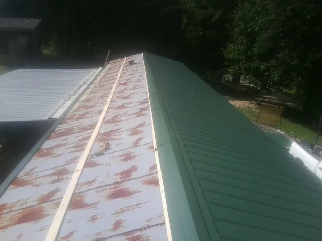 Old rusted panels beside newly installed green metal roofing — Wind Damage Roof Repair by Roofing Brothers in Bath Springs