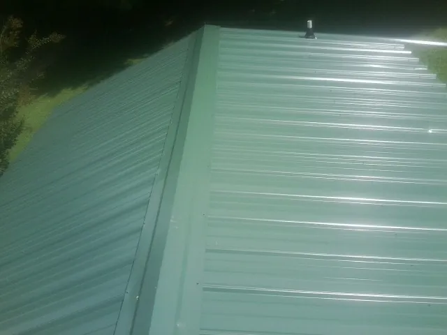 New green metal panels meeting at the ridge of a roof — Flat Roof Repair work by our crew in Bath Springs