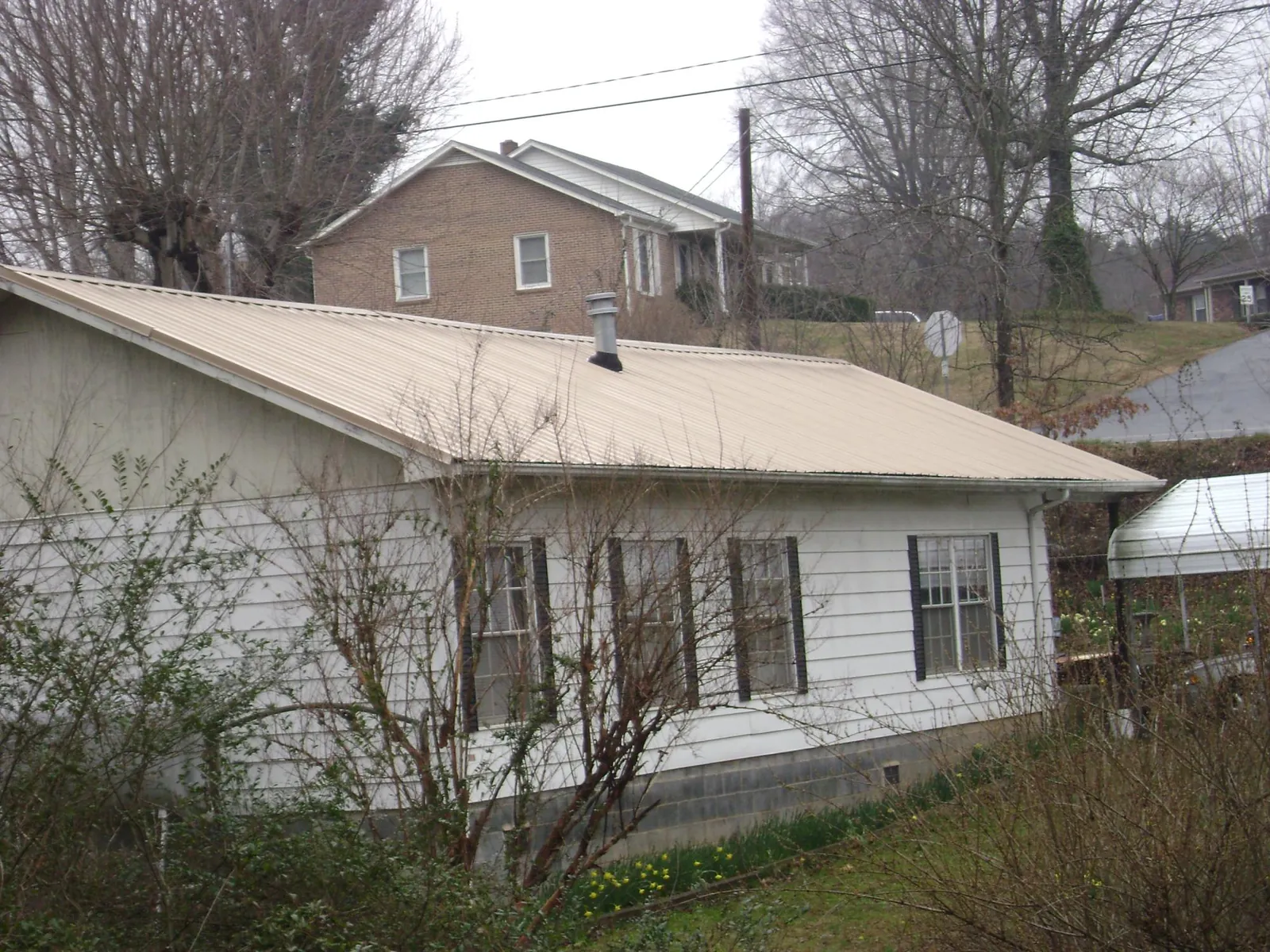 Tan metal roof on a white sided house set into a hillside — Commercial Roofing by Roofing Brothers in Bath Springs