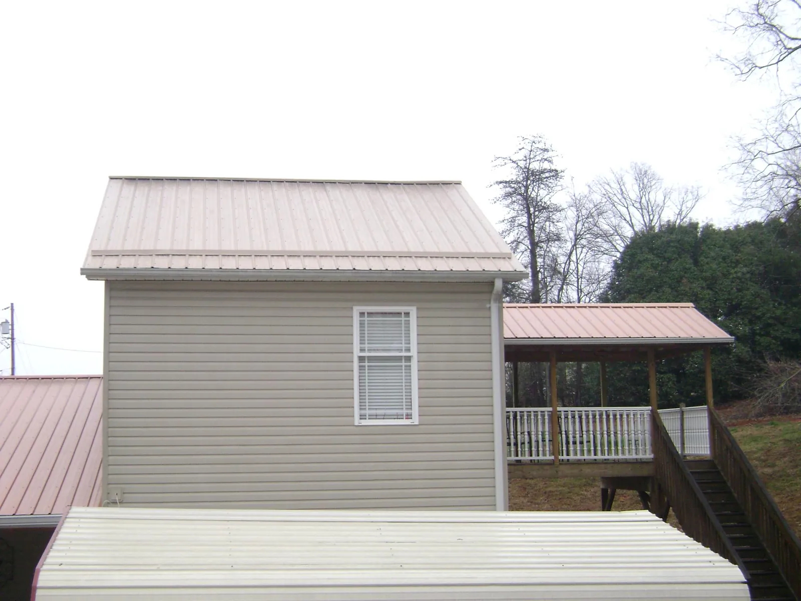 Tan metal roofs on a two story addition and attached porch, from a Roof Replacement job in Bath Springs